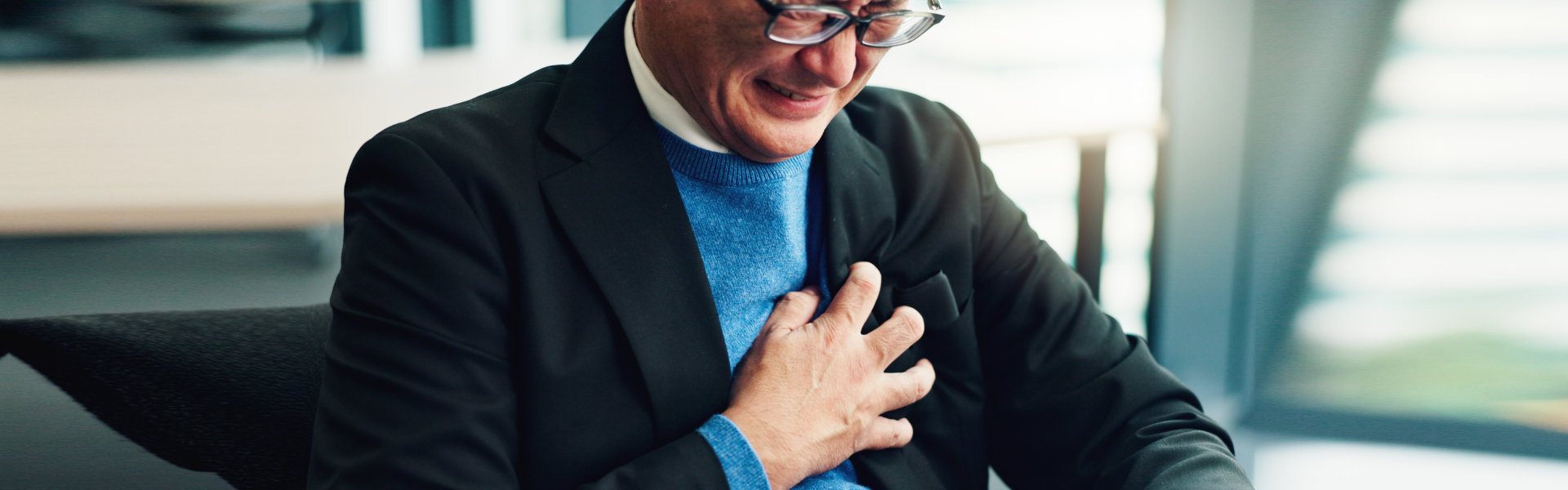 man clutches his chest with a pained expression in an office